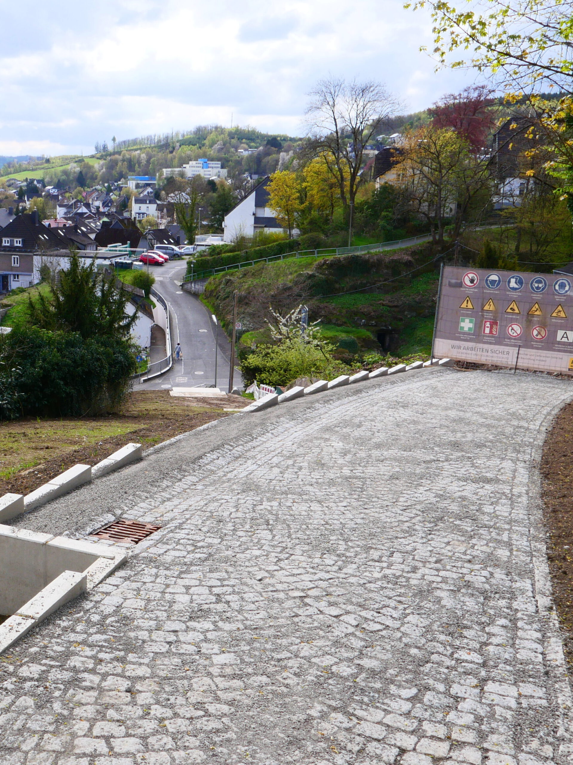 Neu angelegtes Wegstück an einem Hang. Der Weg wird seitlich mit L-Steinen abgestützt und ist durch einen Bauzaun mit Banner abgesperrt.